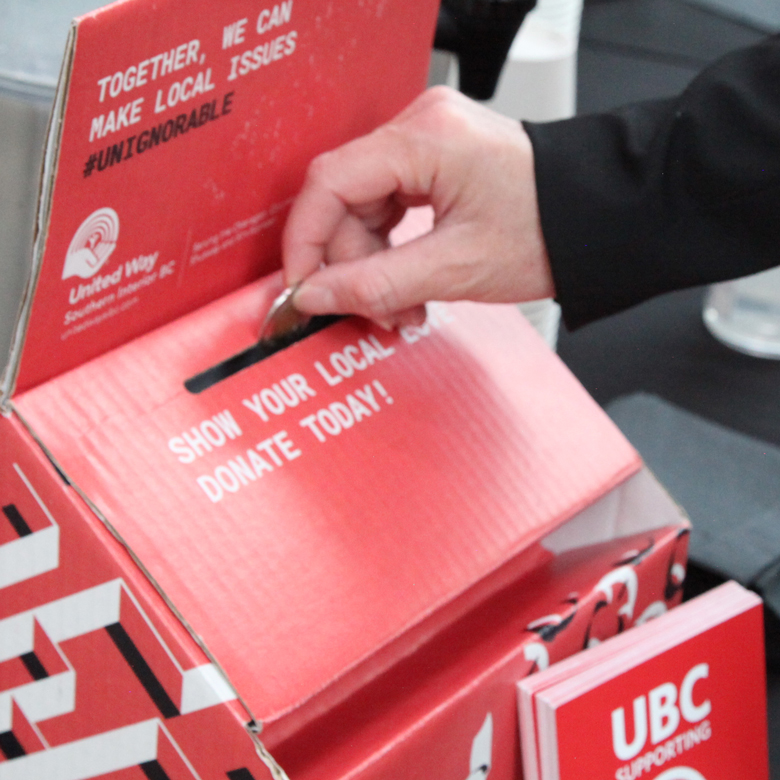 A hand placing a donation in a United Way box